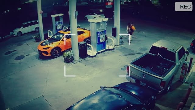CCTV-style shot of an orange car at a gas station at night